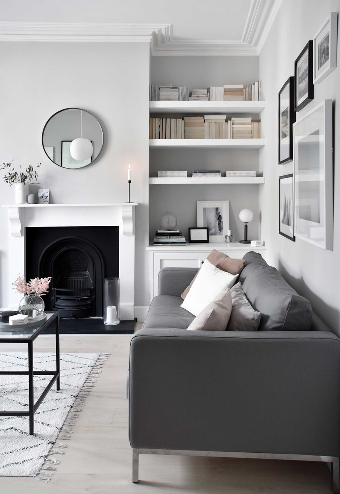 Cette photo montre un salon scandinave de taille moyenne et fermé avec un mur gris, parquet clair, une cheminée standard, un manteau de cheminée en bois, un téléviseur indépendant et un sol beige.