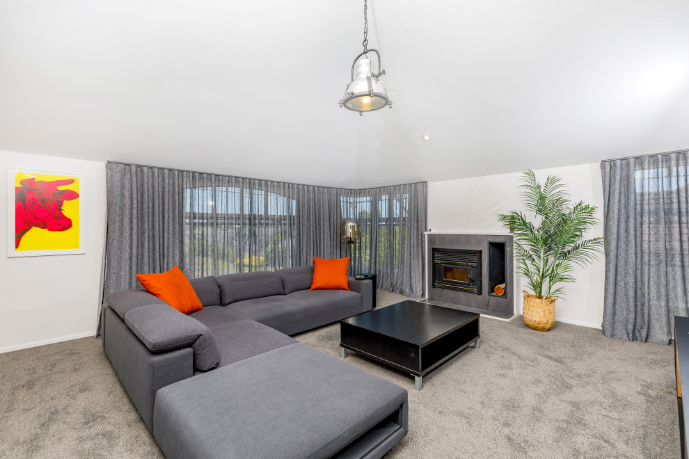 Mittelgroßes, Abgetrenntes Wohnzimmer mit grauer Wandfarbe, Teppichboden, Kaminofen, gefliester Kaminumrandung und grauem Boden in Auckland