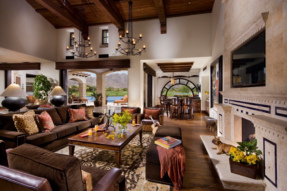 Offenes Mediterranes Wohnzimmer mit beiger Wandfarbe, braunem Holzboden, Kamin und Kaminumrandung aus Stein in Orange County