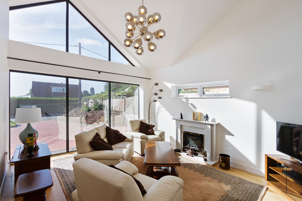 Mid-sized minimalist formal and enclosed laminate floor, brown floor and vaulted ceiling living room photo in West Midlands with white walls, a standard fireplace, a stone fireplace and a corner tv