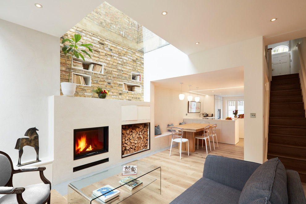 Cette image montre un petit salon design ouvert avec un mur blanc, parquet clair, un manteau de cheminée en plâtre, aucun téléviseur et une cheminée standard.