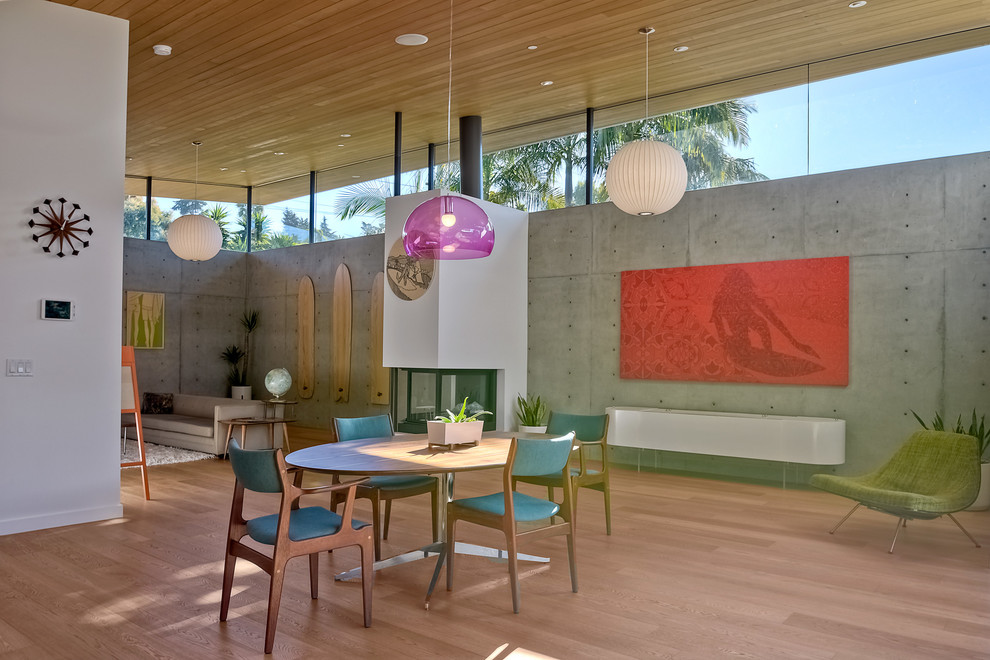Diseño de comedor moderno con paredes blancas, suelo de madera en tonos medios, chimenea de doble cara y marco de chimenea de yeso