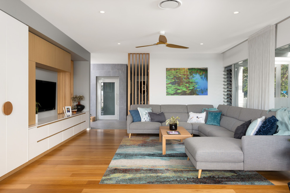 Cette image montre un grand salon design ouvert avec un mur blanc, un sol en bois brun, un téléviseur encastré, un sol marron, poutres apparentes et aucune cheminée.