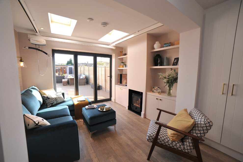 Cette image montre un petit salon design ouvert avec une salle de réception, un mur rose, sol en stratifié, un poêle à bois, un manteau de cheminée en plâtre, un téléviseur indépendant et un sol marron.