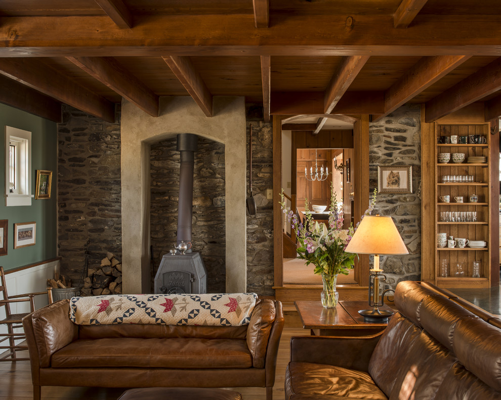 Foto di un soggiorno tradizionale chiuso con pareti verdi, pavimento in legno massello medio, stufa a legna e cornice del camino in intonaco