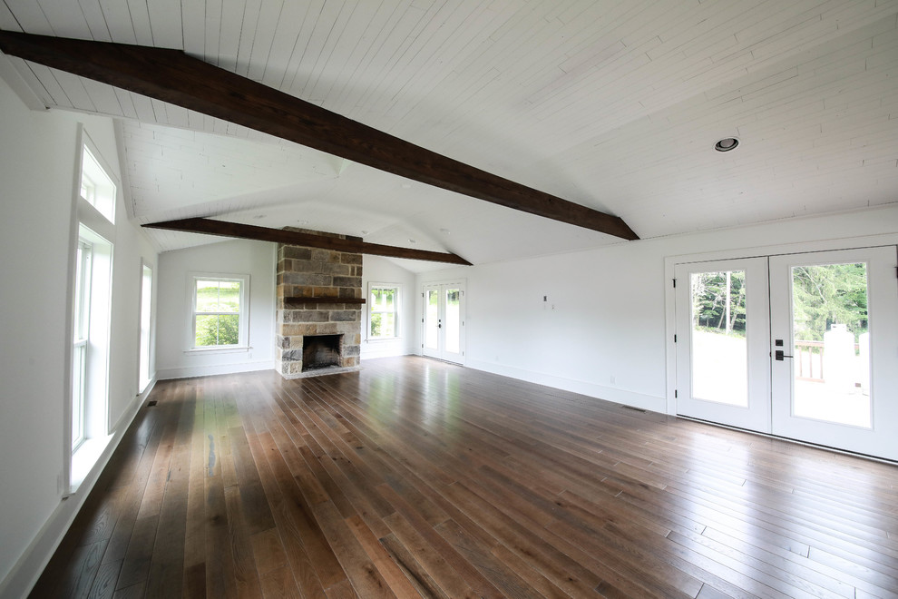 Cette photo montre un salon nature avec un mur blanc, un sol en bois brun, une cheminée standard, un manteau de cheminée en pierre et aucun téléviseur.