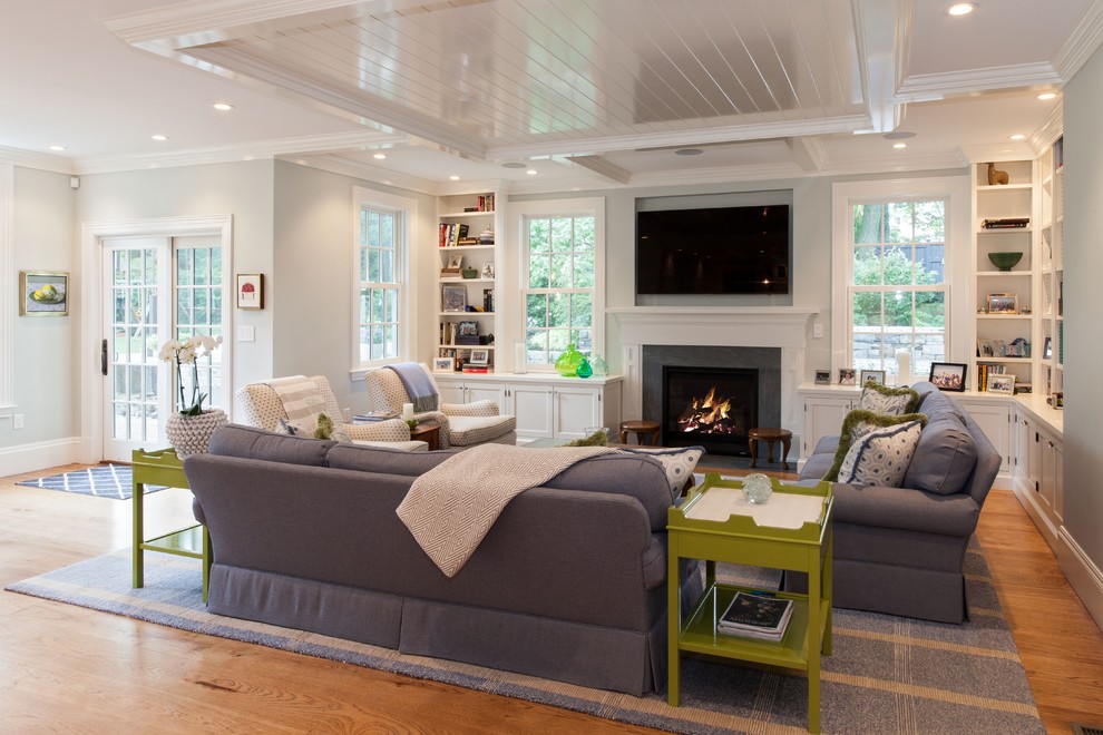 Example of a large classic open concept medium tone wood floor and brown floor living room design in Boston with a standard fireplace, a wall-mounted tv, gray walls and a stone fireplace