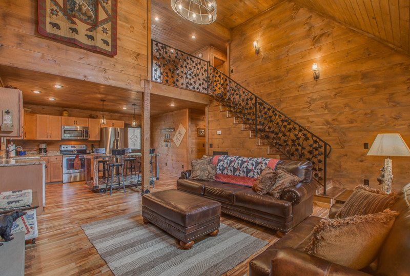 Mid-sized mountain style open concept medium tone wood floor and brown floor living room photo in Nashville with brown walls, a standard fireplace, a stone fireplace and a wall-mounted tv