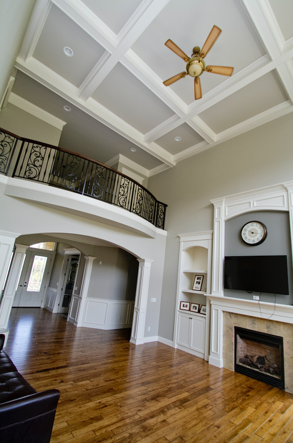 Exemple d'un grand salon tendance ouvert avec un mur gris, un sol en bois brun, une cheminée standard, un manteau de cheminée en carrelage, un téléviseur fixé au mur et un sol marron.