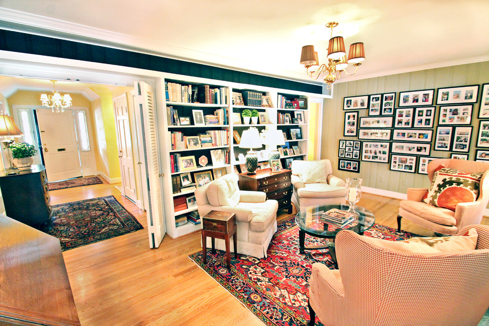 Immagine di un soggiorno chic aperto con libreria, pareti gialle, pavimento in legno massello medio, camino bifacciale, cornice del camino in legno e nessuna TV