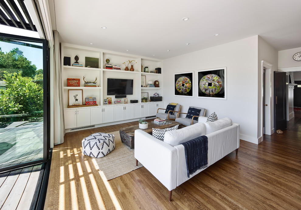 Foto på ett funkis vardagsrum, med vita väggar, mellanmörkt trägolv, en väggmonterad TV och brunt golv