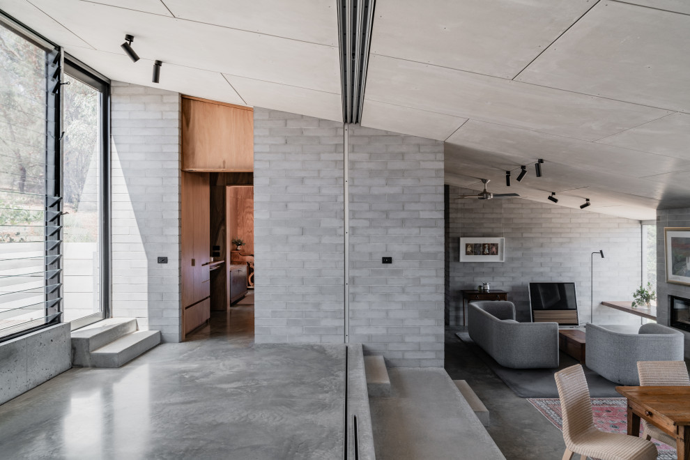 Cette photo montre un grand salon industriel ouvert avec un mur gris, sol en béton ciré, une cheminée standard, un manteau de cheminée en béton, un téléviseur indépendant et un sol gris.