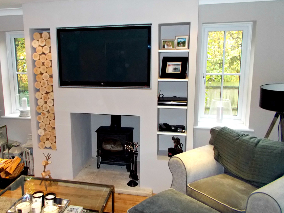 Imagen de salón minimalista con estufa de leña, marco de chimenea de yeso y televisor colgado en la pared