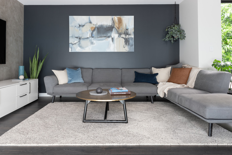 Diseño de salón abierto actual con paredes grises, suelo de madera oscura, televisor colgado en la pared y suelo marrón