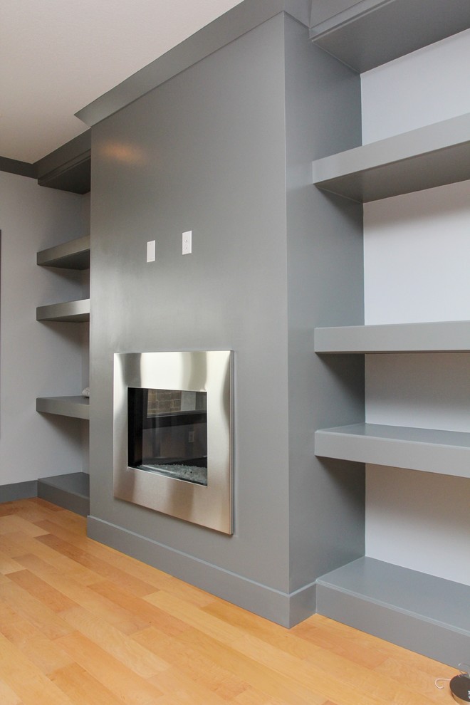 Immagine di un piccolo soggiorno minimalista aperto con pareti grigie, parquet chiaro, camino classico e parete attrezzata