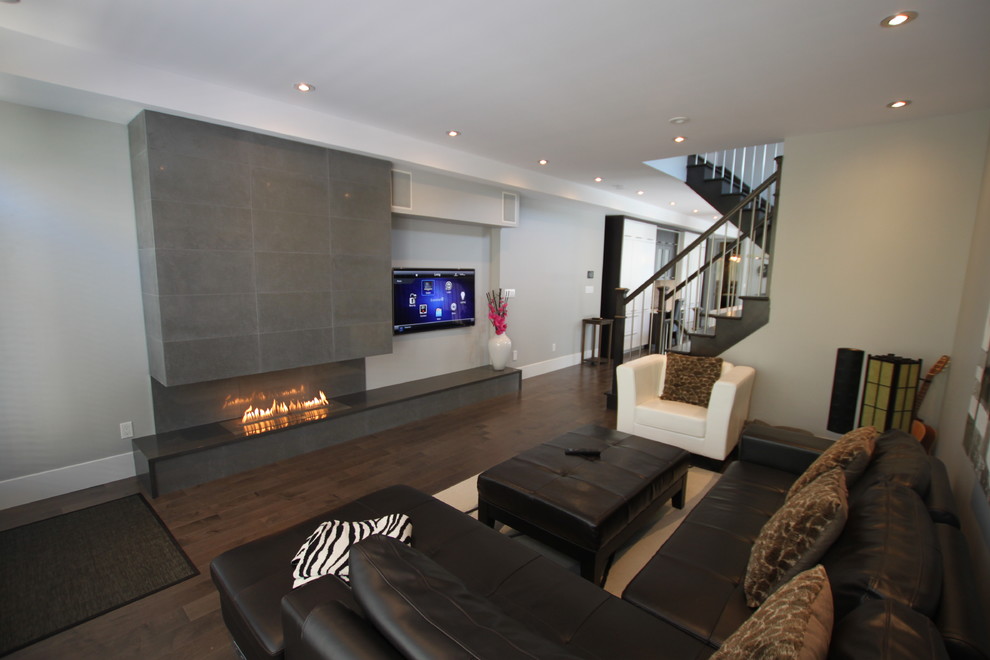 Foto de salón abierto minimalista grande con paredes grises, suelo de madera oscura, todas las chimeneas, marco de chimenea de piedra y televisor colgado en la pared