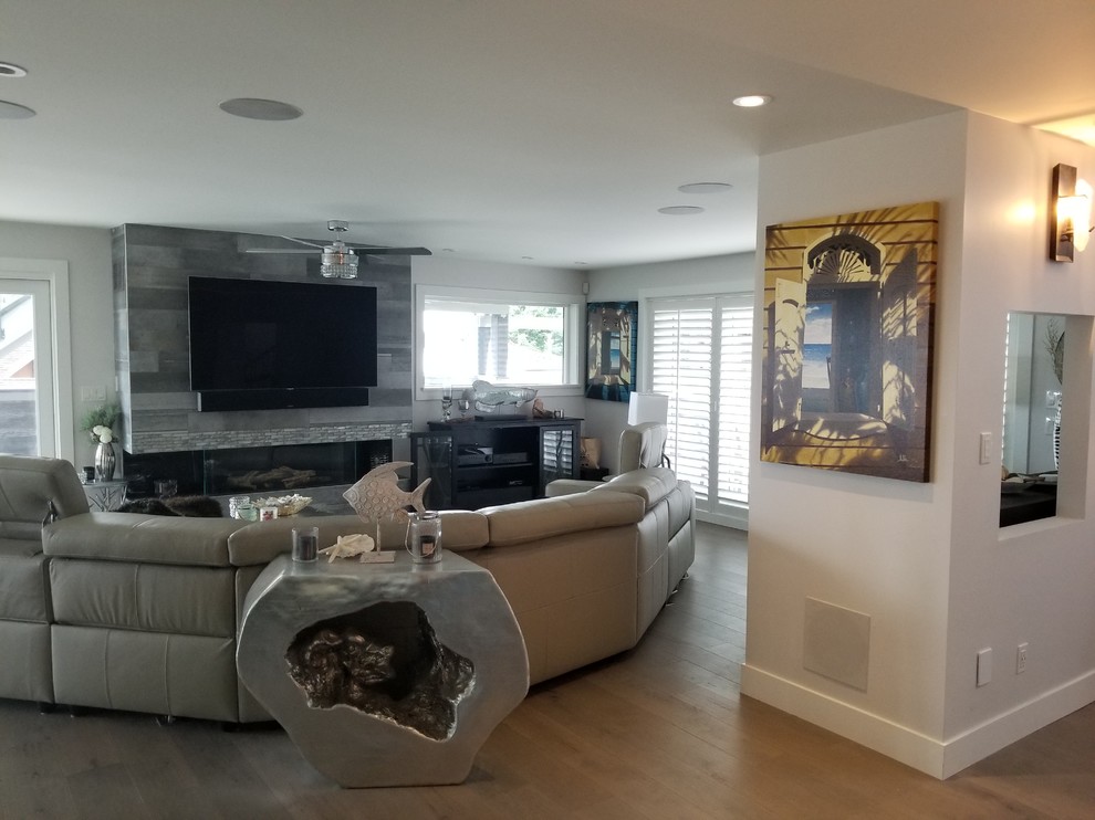 Inspiration for a large coastal open plan living room in Vancouver with grey walls, light hardwood flooring, a standard fireplace, a tiled fireplace surround, a wall mounted tv and grey floors.