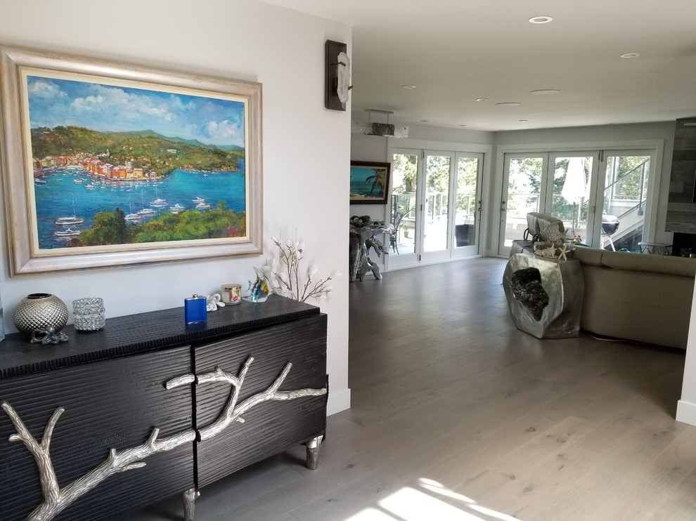 バンクーバーにある高級な広いビーチスタイルのおしゃれなLDK (グレーの壁、淡色無垢フローリング、標準型暖炉、タイルの暖炉まわり、壁掛け型テレビ、グレーの床) の写真