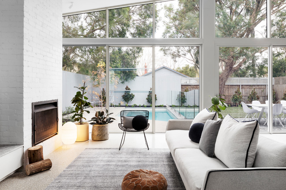 This is an example of a medium sized contemporary living room in Melbourne with concrete flooring, a standard fireplace, a brick fireplace surround, white walls and grey floors.