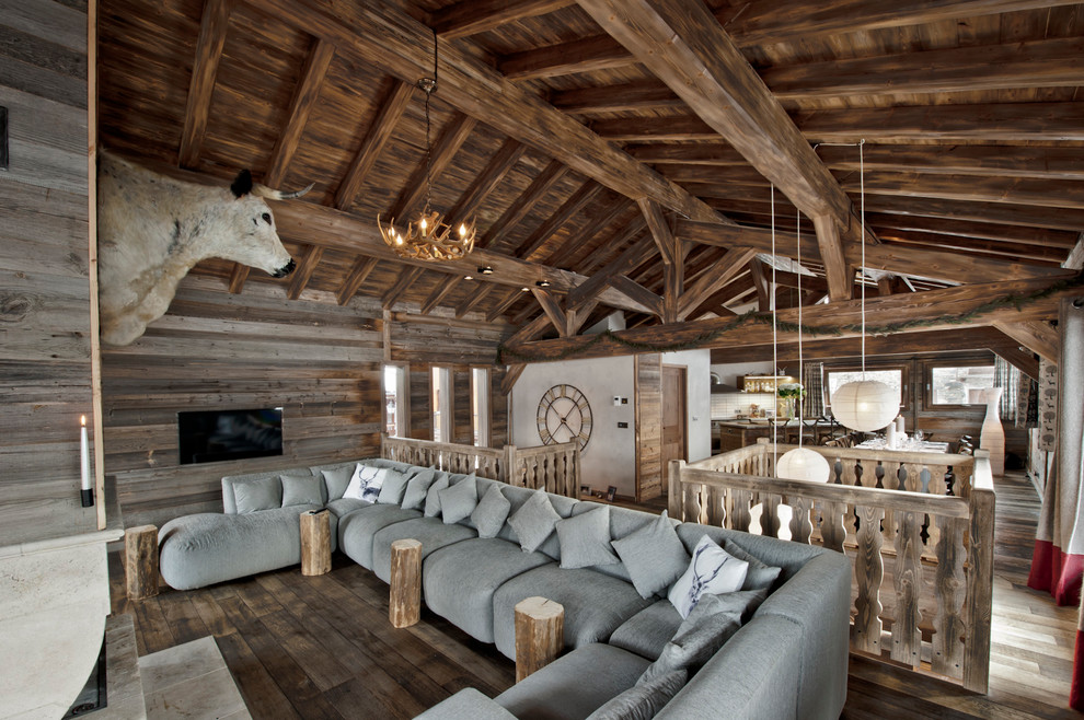 Foto de salón tipo loft rústico grande con suelo de madera en tonos medios, marco de chimenea de piedra y televisor colgado en la pared