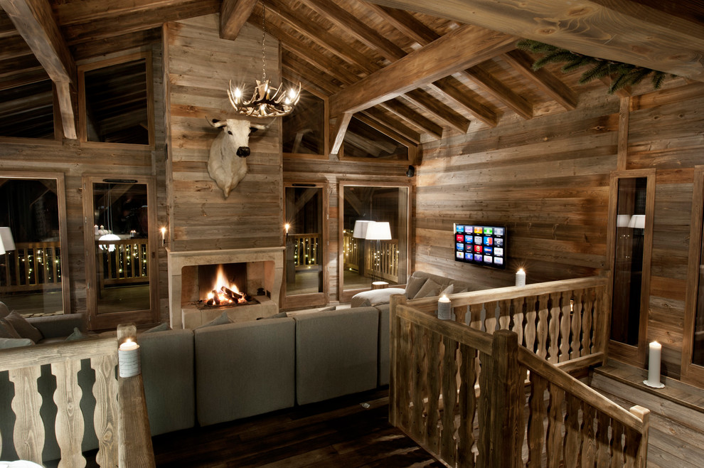 Foto de salón tipo loft rural grande con suelo de madera en tonos medios, marco de chimenea de piedra y televisor colgado en la pared