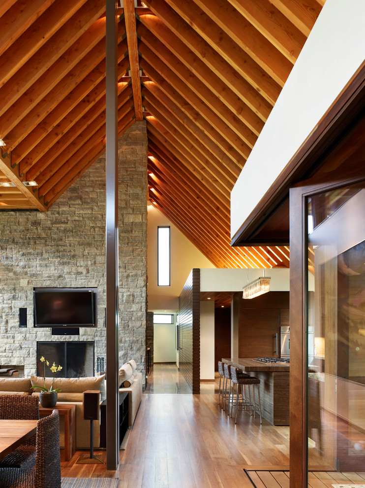 Immagine di un grande soggiorno minimal stile loft con pareti marroni, pavimento in legno massello medio, cornice del camino in pietra e TV a parete