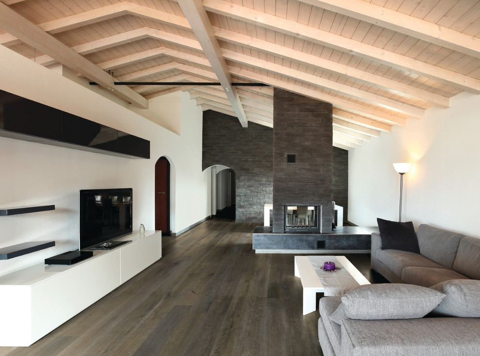 Ejemplo de salón abierto contemporáneo grande con paredes beige, suelo de madera oscura, chimenea de doble cara, marco de chimenea de piedra y televisor independiente