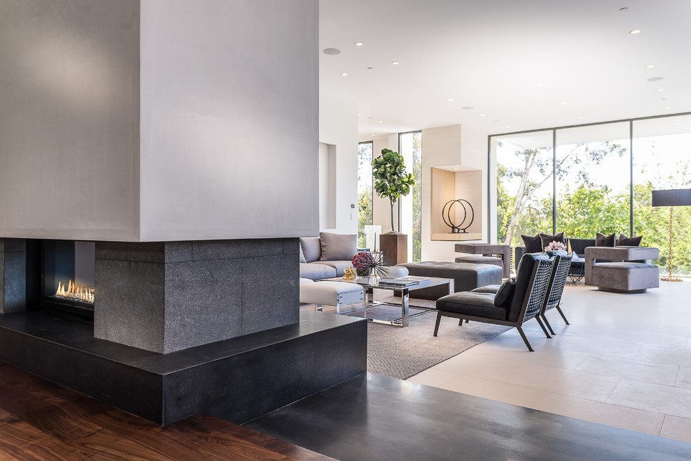 Large modern formal open plan living room in Los Angeles with white walls, limestone flooring, a two-sided fireplace and a stone fireplace surround.