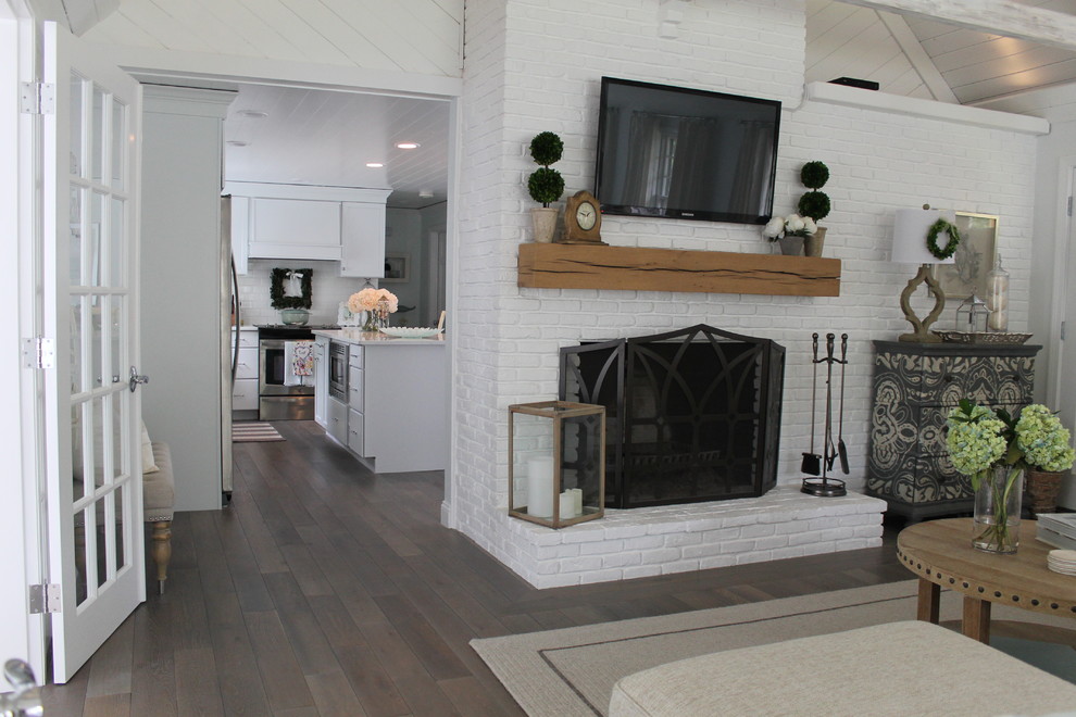 На фото: открытая гостиная комната среднего размера в морском стиле с белыми стенами, темным паркетным полом, стандартным камином, фасадом камина из кирпича и телевизором на стене
