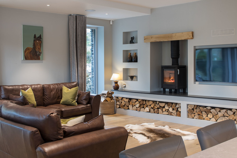 Inspiration pour un salon traditionnel avec un mur gris, parquet clair, un poêle à bois, un téléviseur fixé au mur et un sol beige.