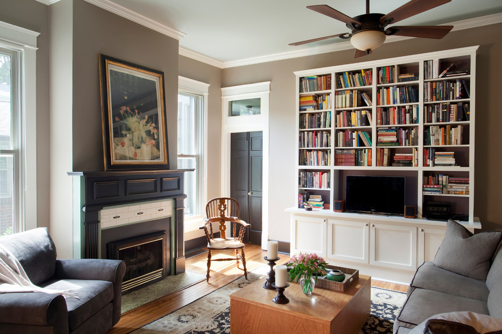 Ejemplo de biblioteca en casa abierta clásica con paredes grises, suelo de madera clara, todas las chimeneas, marco de chimenea de baldosas y/o azulejos y pared multimedia