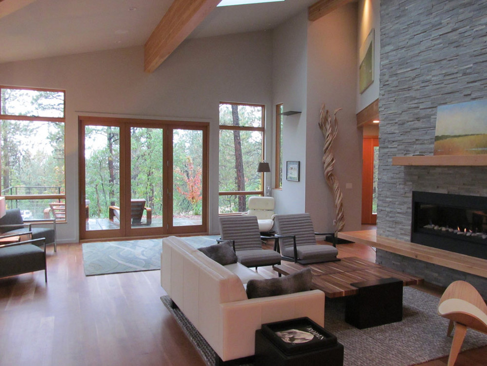 This is an example of an expansive contemporary open plan living room in Albuquerque with white walls, medium hardwood flooring, a ribbon fireplace, a stone fireplace surround and brown floors.