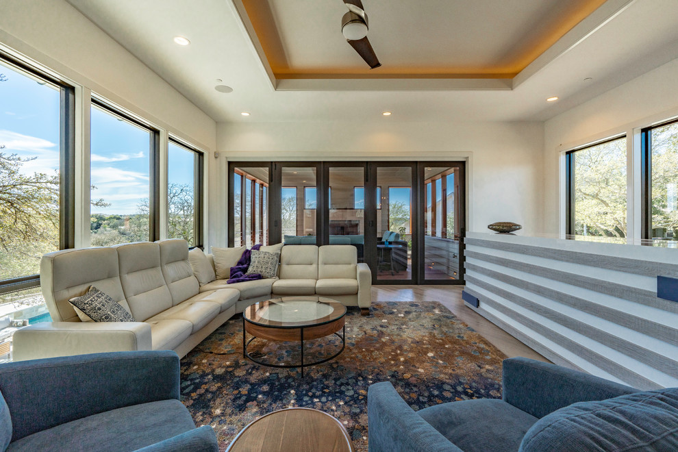This is an example of a large contemporary open plan living room in Austin with white walls, light hardwood flooring, a concealed tv and brown floors.