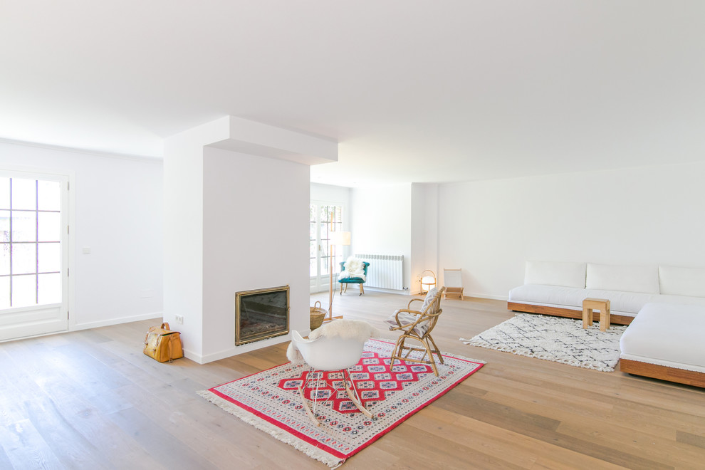 Modelo de salón para visitas abierto escandinavo grande sin televisor con paredes blancas, suelo de madera en tonos medios y todas las chimeneas
