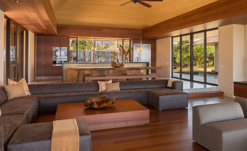 Ejemplo de salón abierto tropical grande con suelo de madera oscura, paredes beige, televisor independiente y suelo marrón