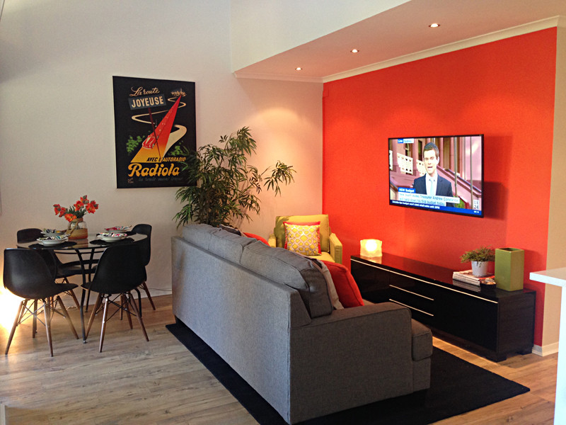 Mittelgroßes, Offenes Modernes Wohnzimmer mit oranger Wandfarbe, Bambusparkett und TV-Wand in Brisbane