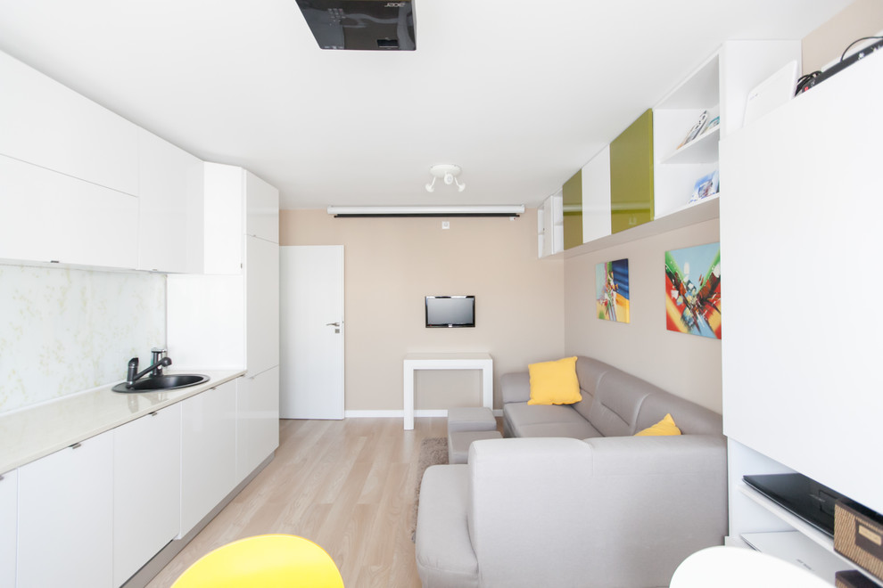 Modelo de salón abierto actual pequeño sin chimenea con paredes beige, suelo de madera clara y televisor independiente