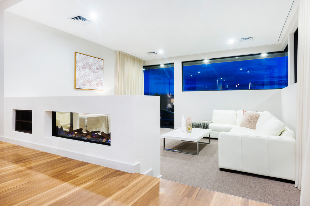 Modelo de salón para visitas abierto contemporáneo pequeño con paredes blancas, moqueta, chimenea de doble cara, marco de chimenea de yeso, pared multimedia y suelo beige