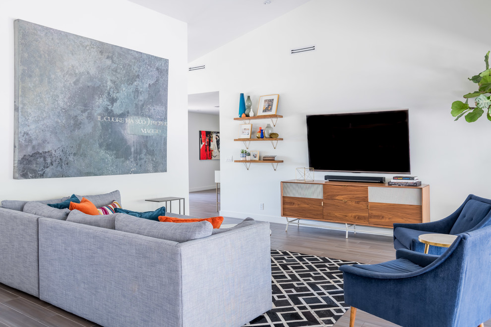 Cette image montre un salon design avec un mur blanc, un sol en bois brun, un téléviseur fixé au mur et un sol gris.