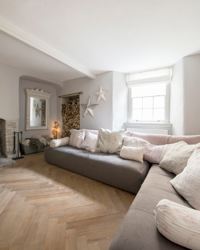 Diseño de salón abierto romántico de tamaño medio con paredes grises, suelo de madera en tonos medios, estufa de leña, marco de chimenea de piedra y televisor retractable