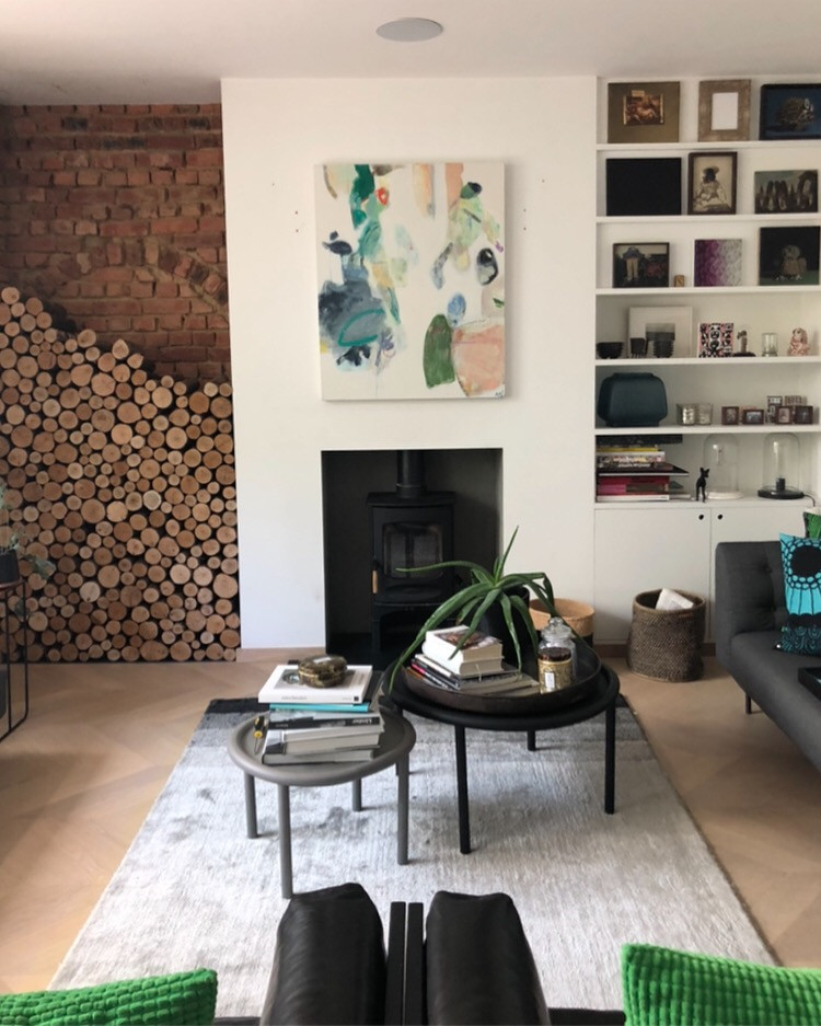 Aménagement d'un salon contemporain avec un mur blanc, parquet clair, un poêle à bois, un manteau de cheminée en plâtre, un sol marron et un mur en parement de brique.