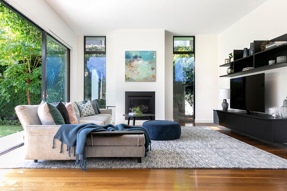 Exemple d'un salon tendance avec un mur blanc, un sol en bois brun, une cheminée standard, un téléviseur indépendant, un sol marron et un manteau de cheminée en pierre.