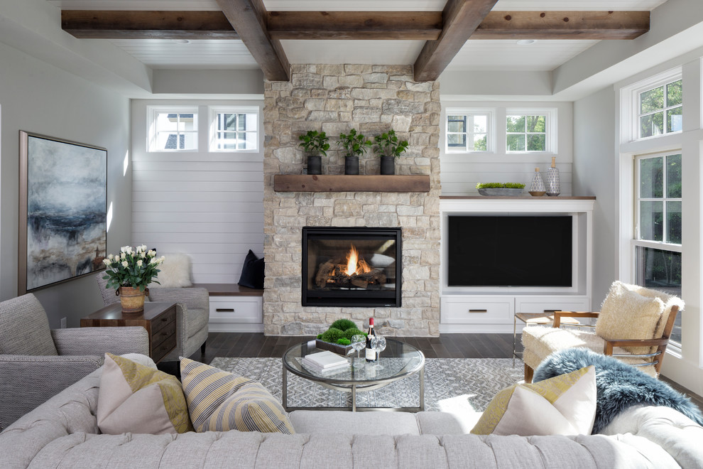 Cette image montre un grand salon traditionnel ouvert avec un mur gris, parquet foncé, une cheminée standard, un manteau de cheminée en pierre, un téléviseur encastré et un sol marron.