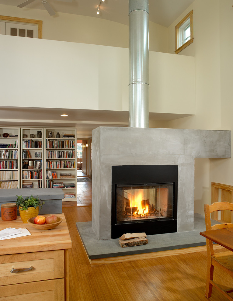 Ejemplo de biblioteca en casa abierta clásica grande con paredes blancas, suelo de madera en tonos medios, estufa de leña, marco de chimenea de hormigón y pared multimedia