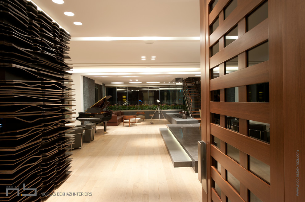 Modelo de salón para visitas abierto actual grande sin chimenea con paredes blancas, suelo de madera clara y pared multimedia