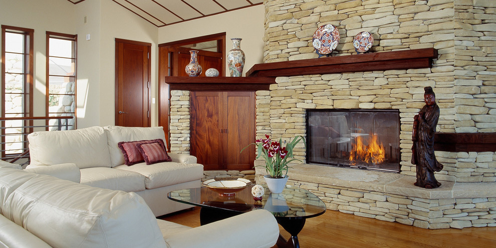 Пример оригинального дизайна: гостиная комната в восточном стиле с стандартным камином и фасадом камина из камня