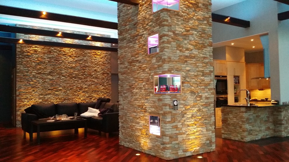 Modelo de salón abierto moderno grande sin chimenea con paredes blancas, suelo de madera en tonos medios y televisor retractable