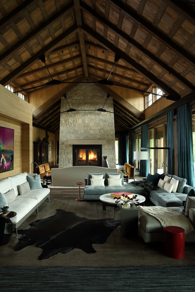 Modelo de salón abierto rústico grande con paredes marrones, suelo de madera en tonos medios, chimenea de doble cara, marco de chimenea de piedra y suelo gris