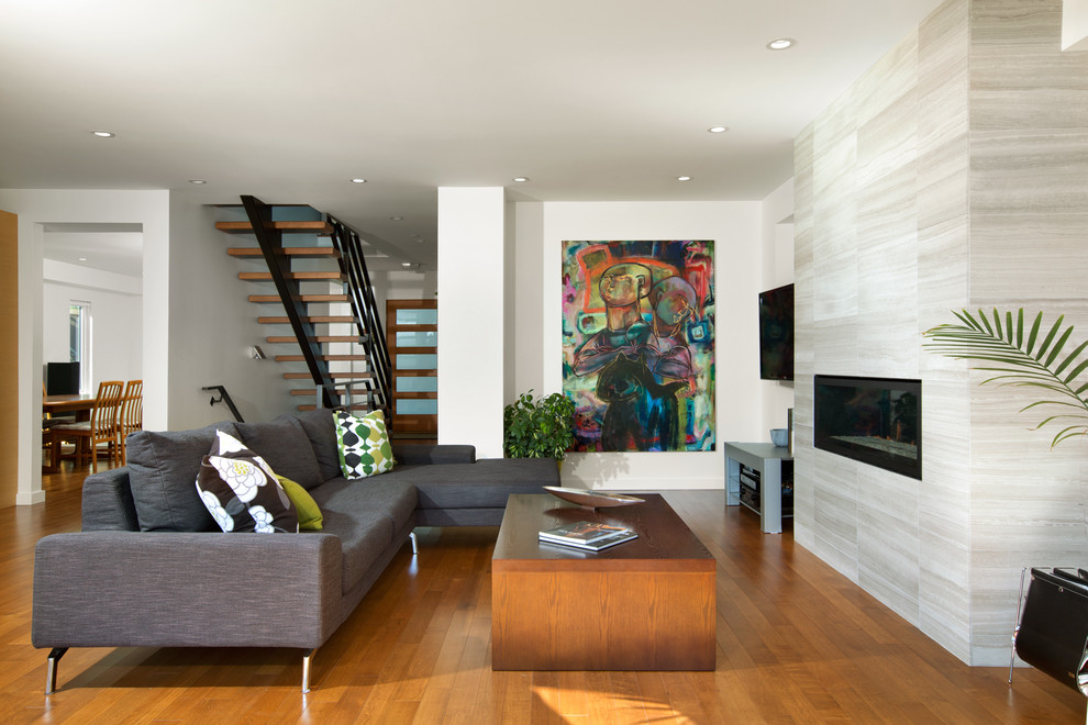 Modelo de salón abierto moderno con paredes blancas, suelo de madera en tonos medios, televisor colgado en la pared, chimenea lineal y marco de chimenea de piedra