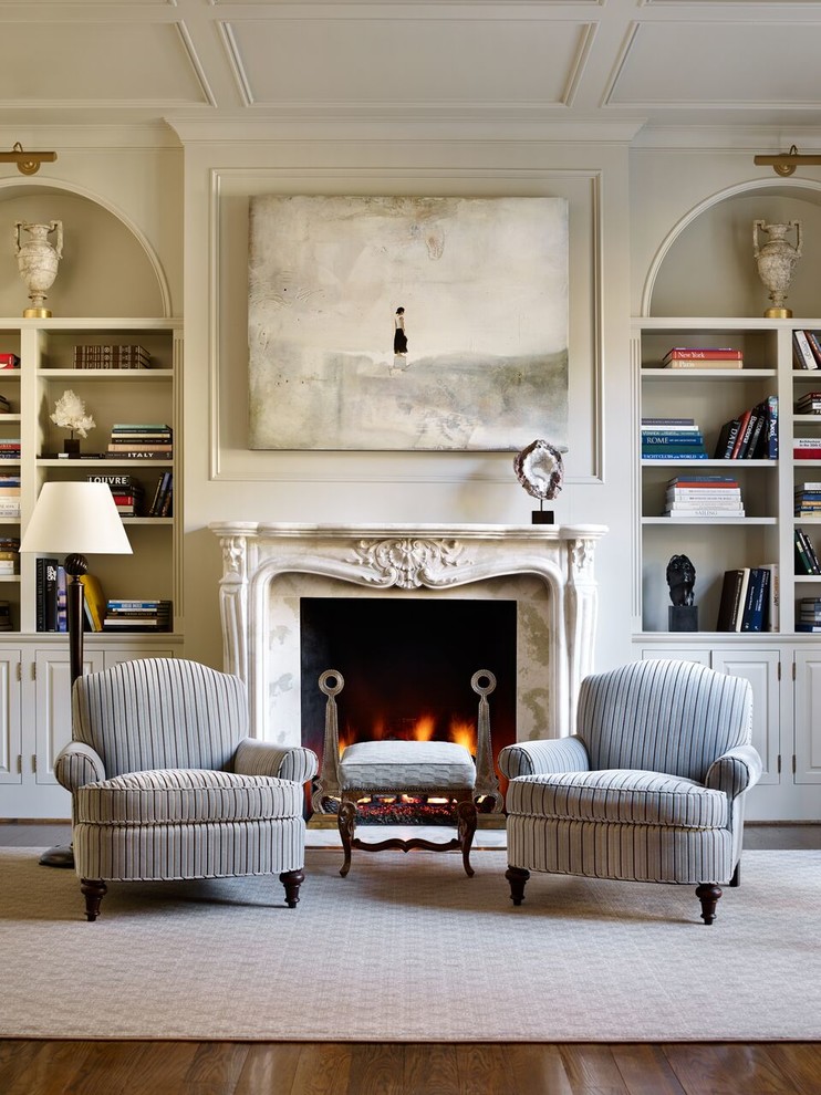 Cette photo montre un salon chic avec une bibliothèque ou un coin lecture, un mur beige et une cheminée standard.